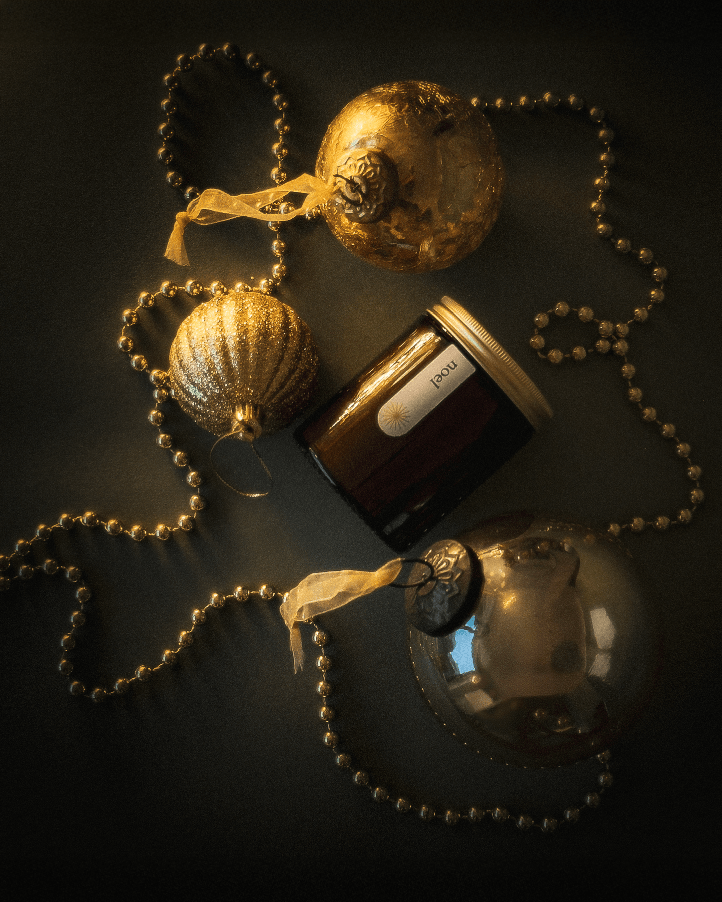 Noel candle surrounded by gold baubles and beads looking down from above.